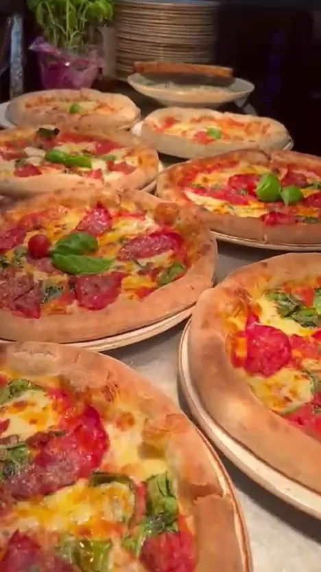 Nystekt pizza løftes ut av steinovnen